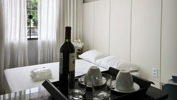 A hotel room with a bed, a bedside table with a bottle of wine, glasses, and a tray. - Aeroband (Núcleo Bandeirante)