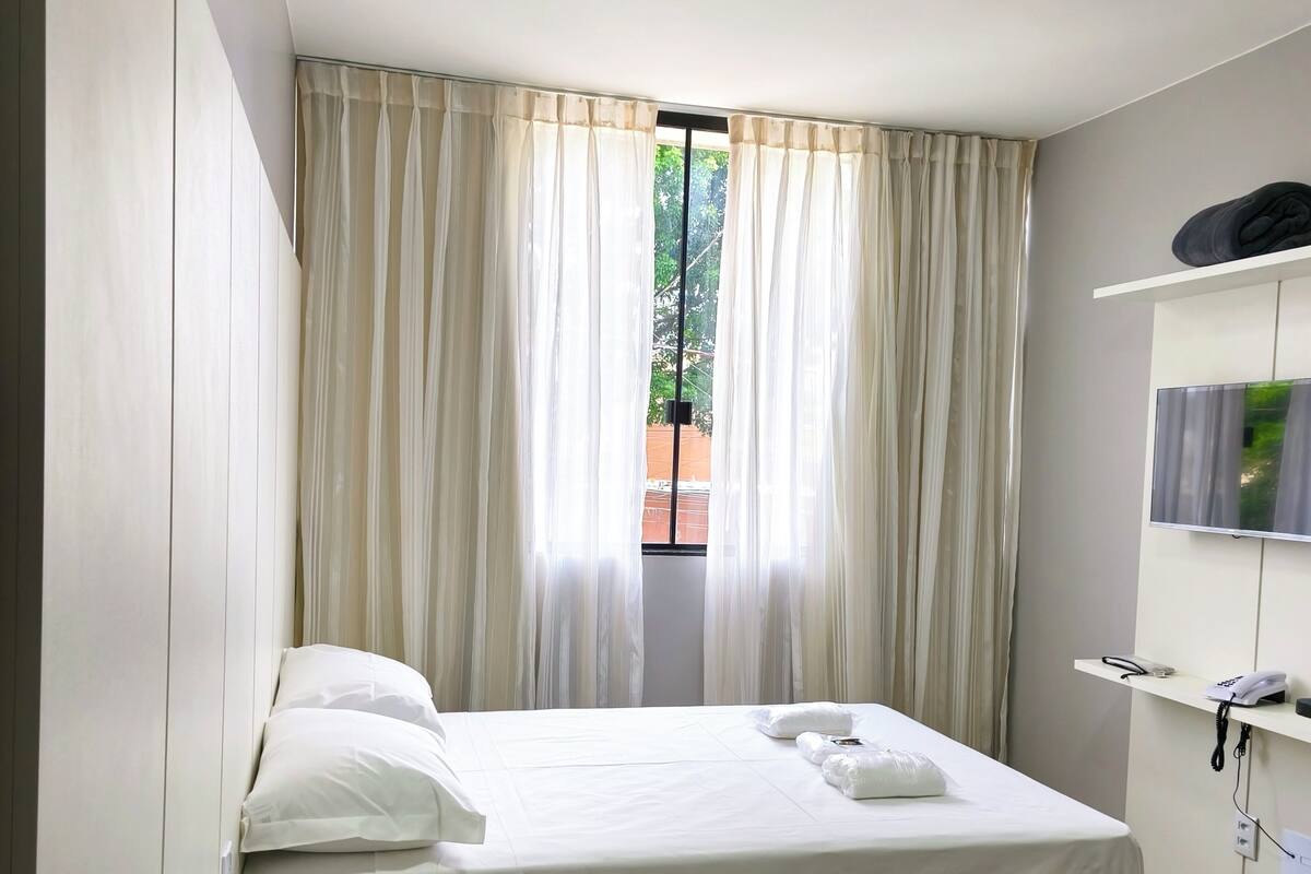 Une chambre d’hôtel équipée d’un lit, d’un bureau, d’une chaise, d’une télévision et d’une fenêtre avec des rideaux.