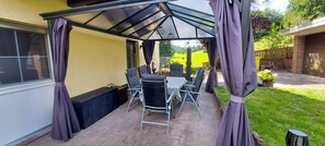 A covered patio area with a table and chairs, a window, and a view of a green field. - Rehblick apartment in the Odenwald hiking and mountain biking paradise (Fürth)