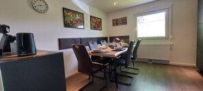 A modern dining area with a wooden table set for four, surrounded by black chairs. A coffee machine is on the left, and there are two wall-mounted clocks. - Rehblick apartment in the Odenwald hiking and mountain biking paradise (Fürth)