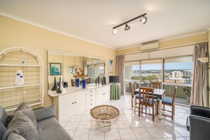 A living room with a sofa, a coffee table, a dining table with chairs, a TV, and a balcony with a view. - Apartment 'Candirocha C9' (Portimão)