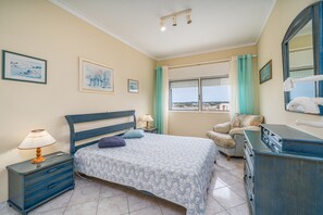A bedroom with a bed, a nightstand, a dresser, a chair, a window with curtains, and artwork on the walls. - Apartment 'Candirocha C9' (Portimão)