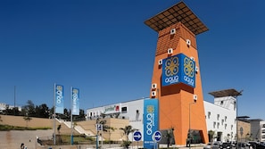 A modern building with a prominent tower, banners, and a parking sign.