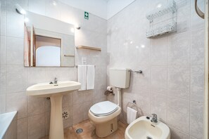 Un baño con lavamanos pedestal, inodoro, bidé y espejo.