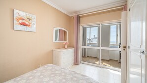 Quarto com cama, penteadeira, espelho e porta de correr para uma varanda.