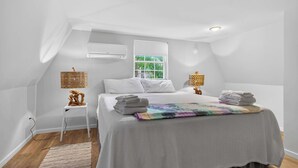 A bedroom with a bed, a window, an air conditioner, and a small table with a lamp. - 401 142nd Street (Ocean City)