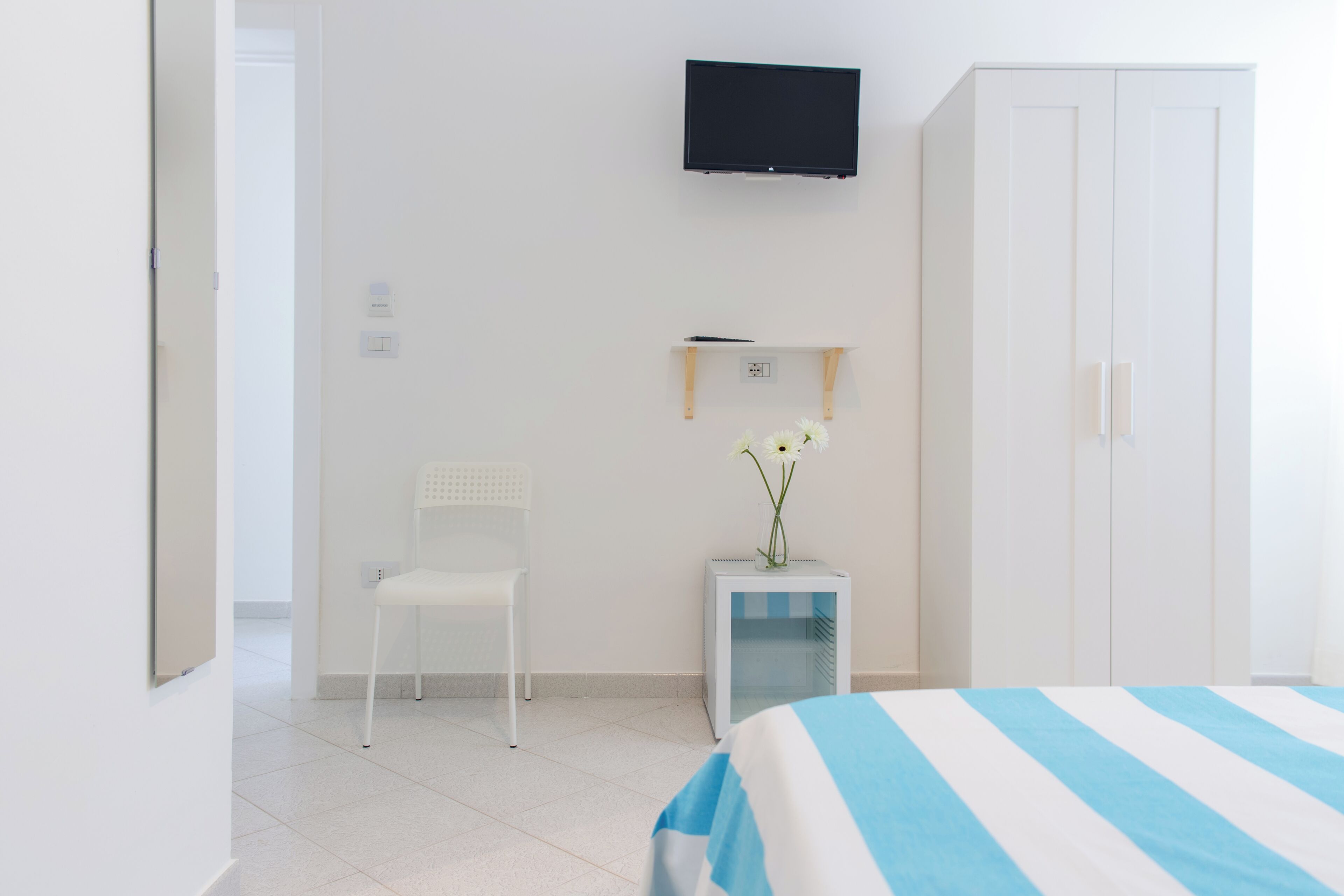 Une chambre d’hôtel comprenant un lit, un téléviseur fixé au mur, une chaise, une petite table avec un vase et une armoire.
