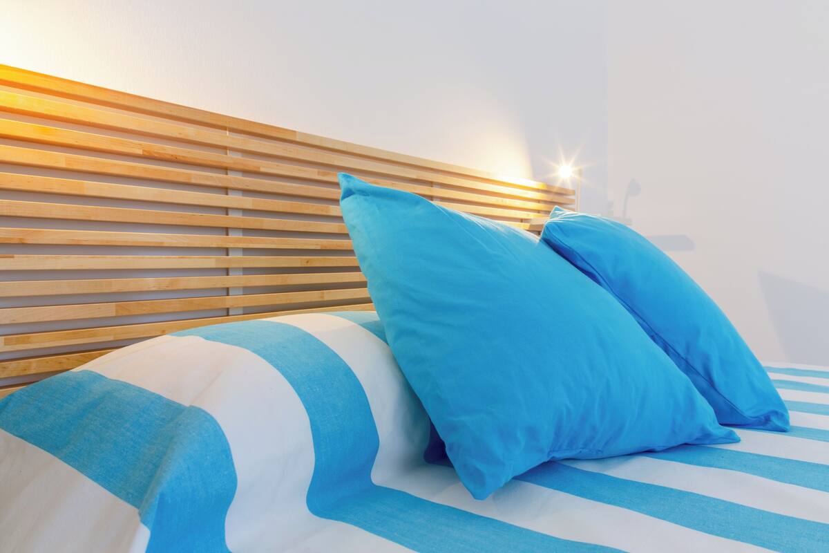 A bed with blue and white striped bedding, two blue pillows, and a wooden headboard.