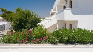 Un edificio blanco con balcones, rodeado de arbustos verdes y flores rosadas.