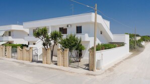 A modern white building with a gated entrance, a clear sky, and a paved road. - Vidamarina - Camere al Mare (Torre Castiglione)