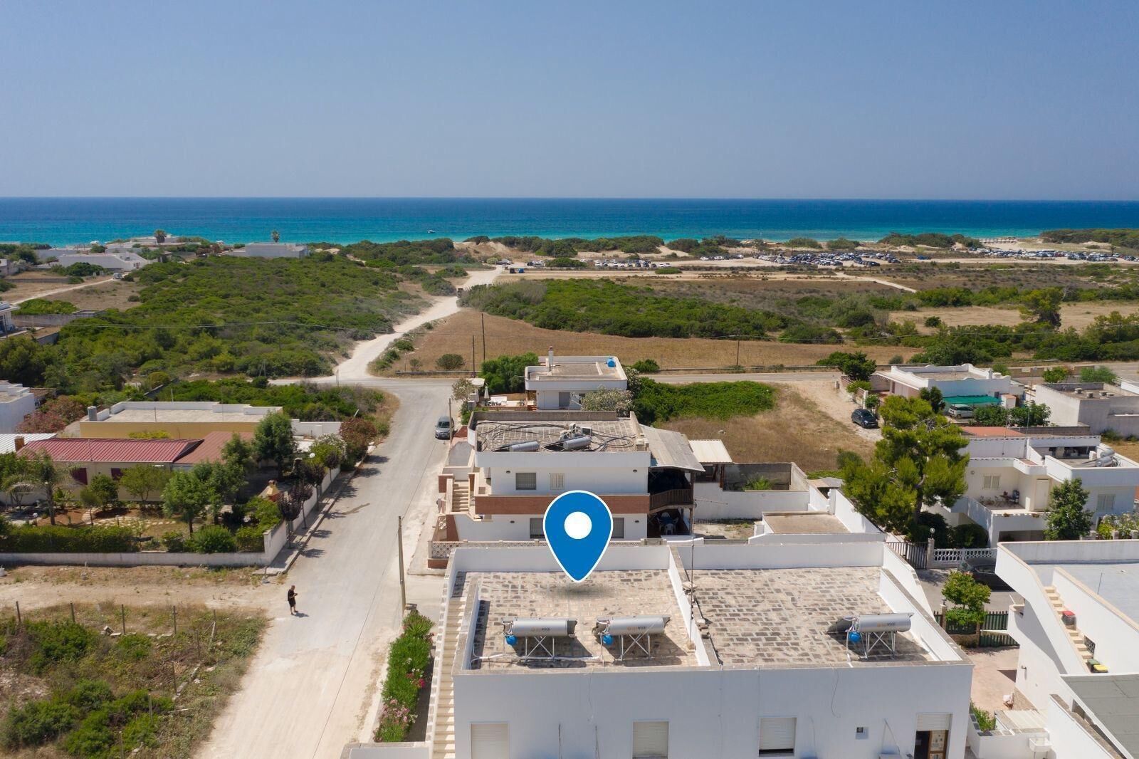 An aerial view of a coastal residential area with buildings, a road, and a beach in the background.