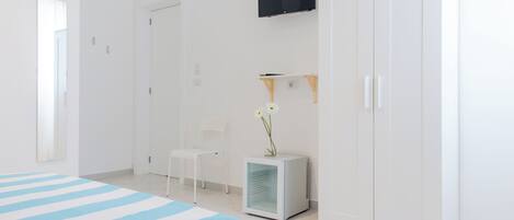 A hotel room with a bed, a TV, a wardrobe, a chair, and a small table with a flower.