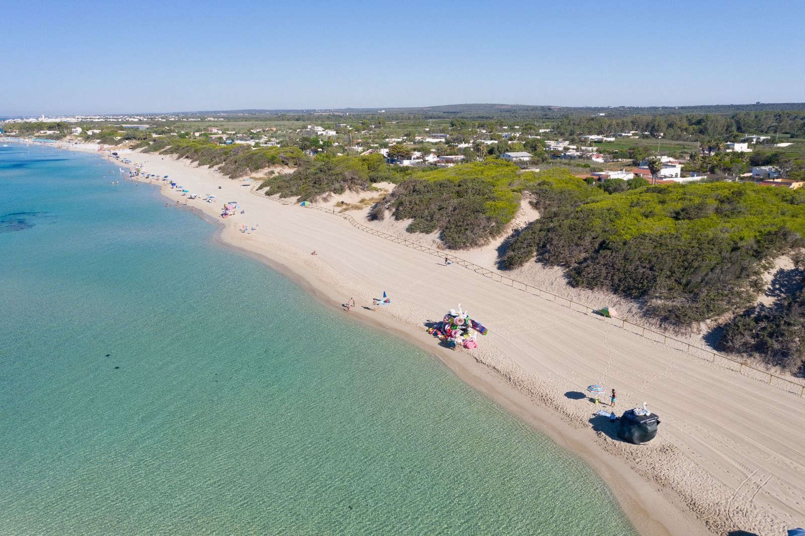 Vista aérea de uma praia com águas cristalinas, areal arenoso e guarda-sóis espalhados.
