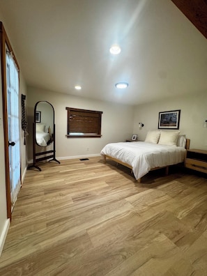 A bedroom with a bed, a mirror, a window with blinds, and a ceiling light.