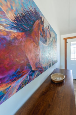 Una habitación con un cuadro abstracto grande en la pared, una mesa de madera y una puerta al fondo.