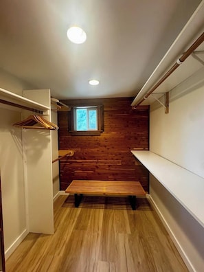 A narrow hallway with wooden flooring, a bench, a coat rack, and a window with a view of greenery.