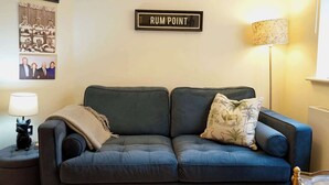 A living room with a dark blue sofa, a lamp, a framed sign reading 'RUM POINT,' and a wall-mounted photo.