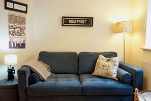 Ein Wohnzimmer mit einem dunkelblauen Sofa, einer Lampe, einem gerahmten Schild mit der Aufschrift 'RUM POINT' und einem Wandbild.