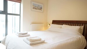 A neatly made bed with white linens and towels, a wooden headboard, a bedside lamp, and a framed picture on the wall.