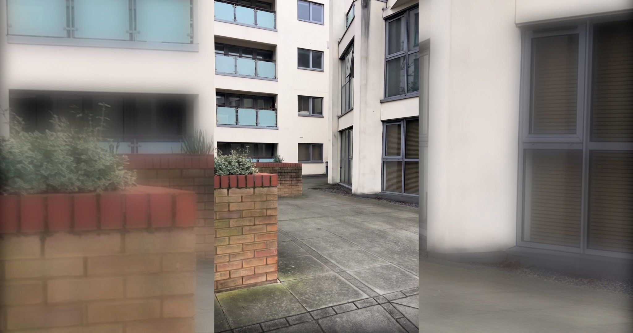 Een meerhoog gebouw met een binnentuin, met een bakstenen muur met beplanting, een betonnen pad en grote ramen.