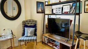A living room with a television, a chair with a patterned cushion, a bookshelf, and a mirror on the wall.