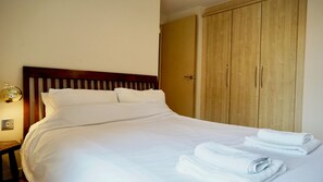 A neatly made bed with white linens, a wooden headboard, and a wooden wardrobe with a door. - Modern 1BDR Flat Opposite Peckham Rye Park (Greater London)