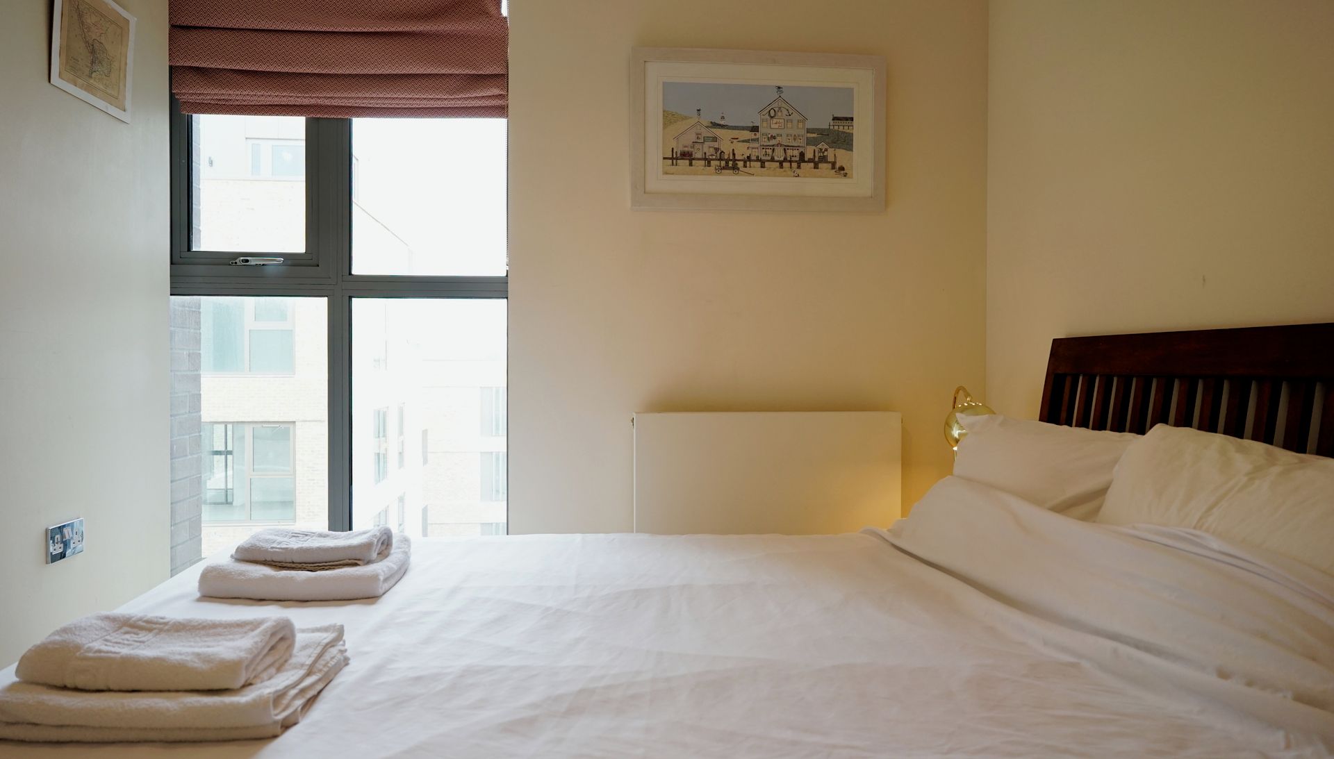 A hotel room with a bed, towels, a window, and a painting on the wall.