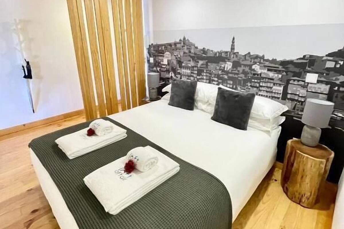 A modern bedroom with a large bed, a cityscape mural, wooden beams, and a wooden nightstand.