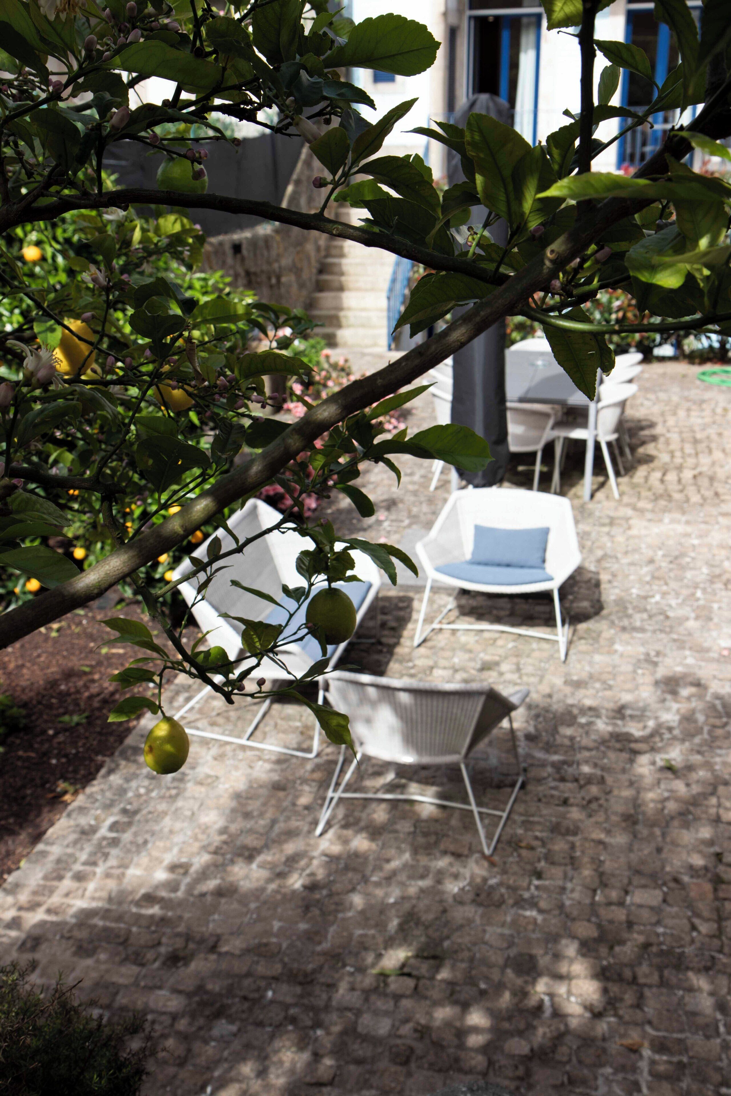An outdoor seating area with white chairs and tables, surrounded by a brick patio and greenery.
