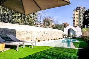 Ein moderner Poolbereich im Freien mit einer Steinwand, Liegestühlen und freiem Blick auf einen Hochhaus im Hintergrund.