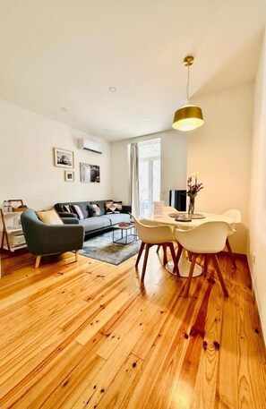 A modern living room with a sofa, a dining table with chairs, and a hanging light fixture. - 1118 Lofts (Porto)
