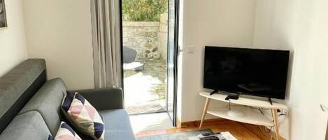 A living room with a grey sofa, a flat-screen TV on a wooden stand, and a small coffee table with magazines.