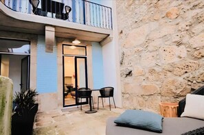 Ein Innenhof mit einer Steinmauer, einem Balkon mit Metallgeländern und einer Sitzgruppe mit zwei Stühlen und einem Tisch.