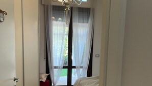 Une chambre à coucher avec un lit, un lustre, une fenêtre avec des rideaux en voile et un plancher en bois.