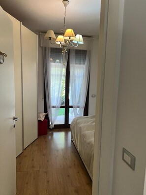A bedroom with a bed, a chandelier, a window with sheer curtains, and a wooden floor. - San rossore area apartment. Ideal for couples, families and business stays (Pisa)