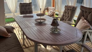 Un patio couvert avec une table en bois, des chaises rembourrées et une vue sur la verdure environnante.