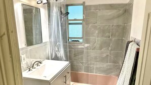 Une salle de bain avec un lavabo blanc, un miroir, un rideau de douche, une baignoire et des murs carrelés.