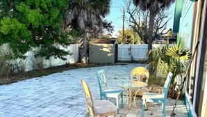 Un espace patio aménagé avec une table et des chaises, entouré d’une clôture blanche et d’arbres.