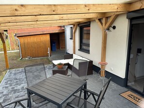Un patio al aire libre con una mesa y sillas, una pérgola de madera, una puerta corrediza y una pequeña planta en maceta.