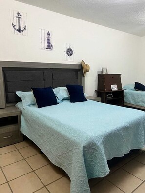 Quarto de hotel com cama, mesa de cabeceira, cômoda e relógio na parede.