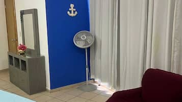 A room with a bed, a red chair, a fan, a mirror, and curtains.