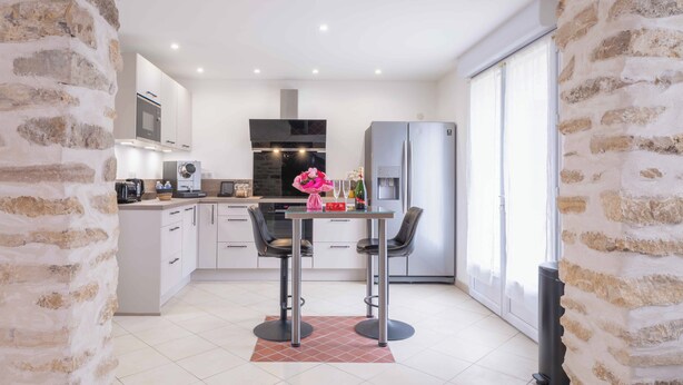A modern kitchen with a stone archway, a dining area with two chairs, and a refrigerator.
