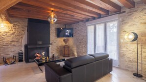 A cozy living room with a stone wall, a fireplace, a black leather sofa, and a TV mounted on the wall.