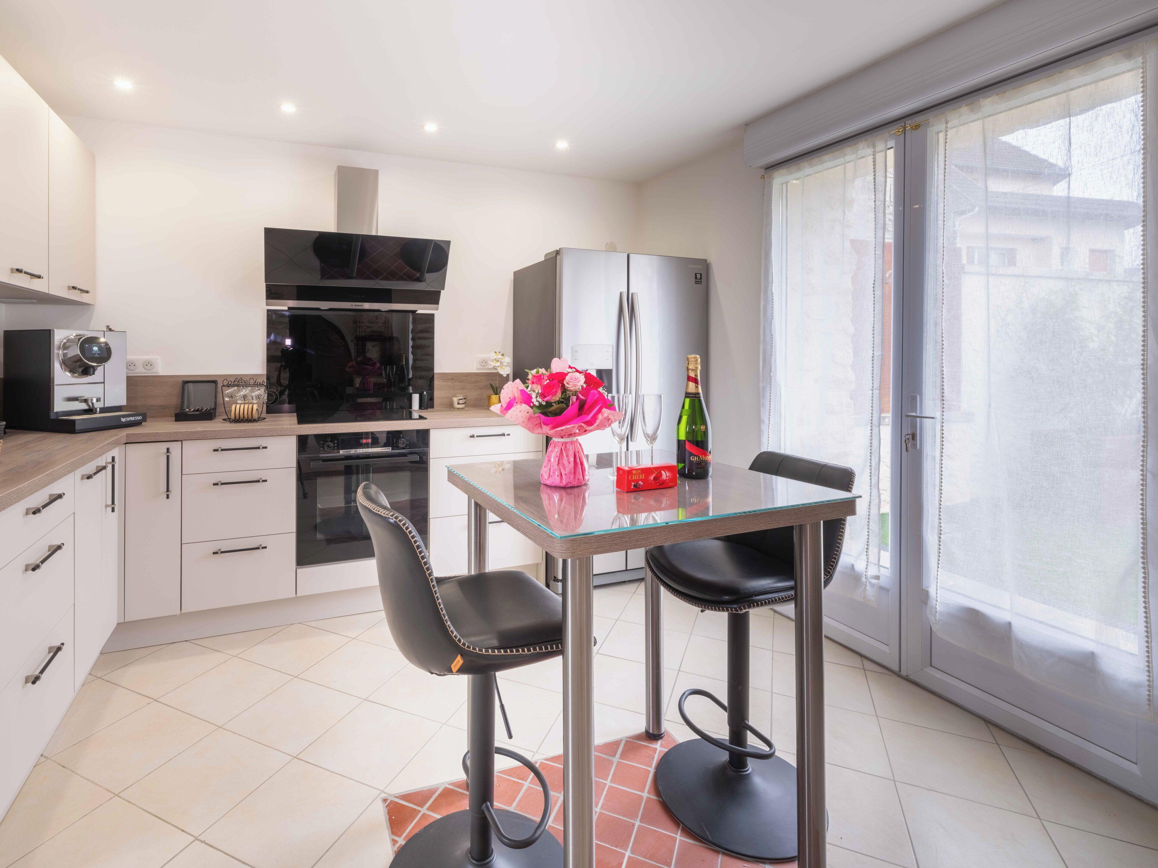 A modern kitchen with a dining area, including a table with chairs, a refrigerator, and a coffee machine.