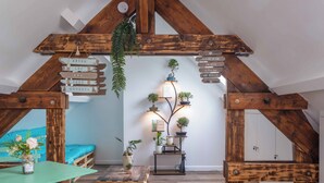 A cozy attic room with a loft bed, a small table with a chair, a wooden coffee table, and a wall-mounted shelf with plants and framed pictures.