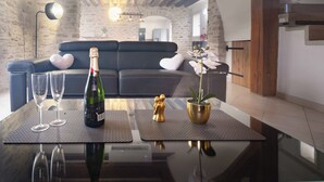 A modern living room with a black leather sofa, a glass coffee table, and a decorative orchid plant.