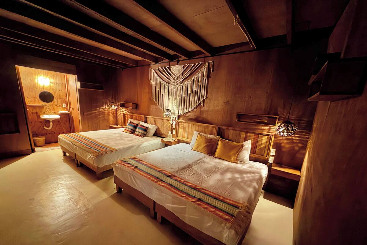 A room with two beds, wooden walls, a hanging light fixture, and a small sink.