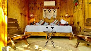 Une pièce en bois avec un lit, deux chaises, une petite table avec des verres et un climatiseur suspendu.