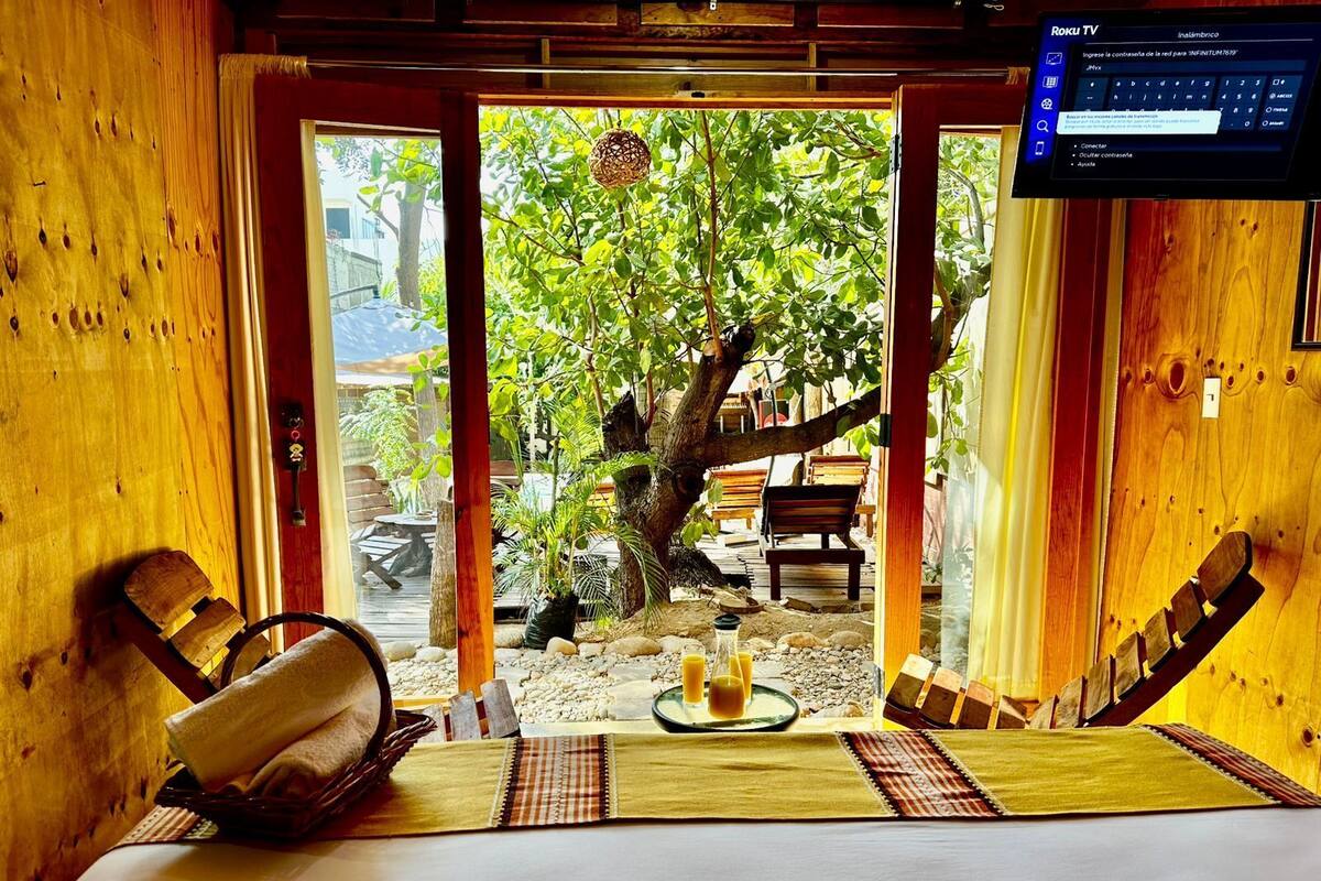 A wooden room with a bed, a table with a tray of drinks, and a TV screen displaying a menu.