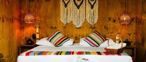 A wooden room with a bed, two wall-mounted lamps, a wall-mounted air conditioner, and a woven macrame wall hanging.